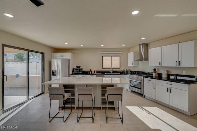 kitchen with wall chimney exhaust hood, stainless steel appliances, sink, a center island, and white cabinetry