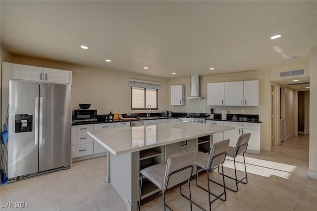 kitchen featuring white cabinets, appliances with stainless steel finishes, a center island, and wall chimney exhaust hood