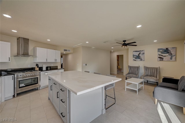 kitchen featuring light stone countertops, wall chimney exhaust hood, high end stove, a kitchen island, and white cabinetry