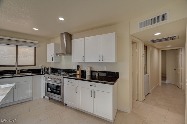 kitchen featuring white cabinets, high end stove, wall chimney range hood, and sink