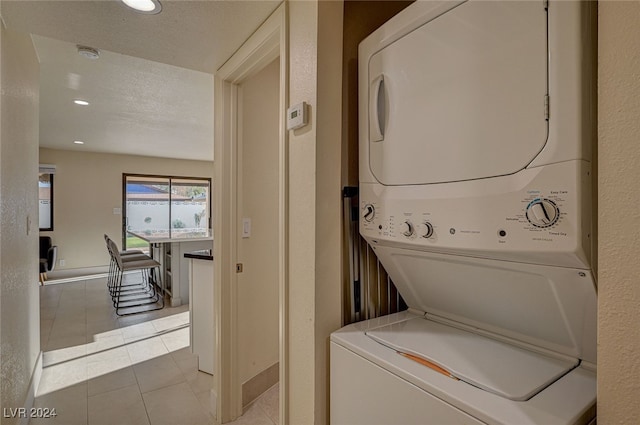 clothes washing area with light tile patterned flooring, stacked washing maching and dryer, and a textured ceiling