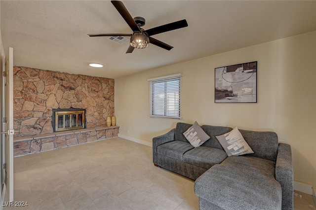 living room with ceiling fan, a stone fireplace, and a textured ceiling