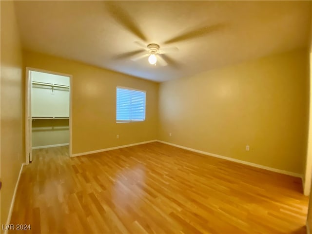 unfurnished bedroom with light wood-type flooring, a spacious closet, ceiling fan, and a closet