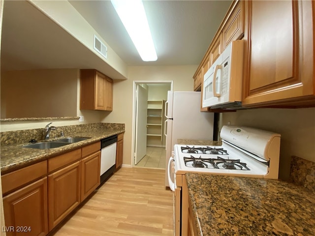 kitchen with dark stone countertops, white appliances, light hardwood / wood-style flooring, and sink