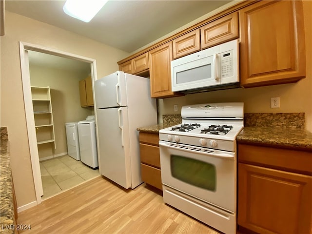 kitchen with light wood-type flooring, white appliances, dark stone counters, and washer and dryer