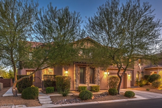 view of front of home with a gate, central AC, concrete driveway, stone siding, and a tile roof