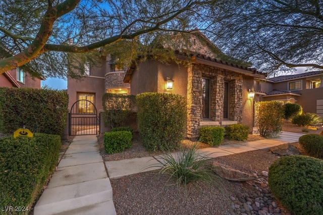 view of front of house featuring stucco siding, stone siding, and a gate