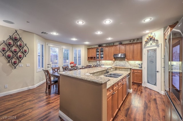 kitchen with a kitchen island with sink, dark wood-type flooring, dishwasher, light stone counters, and sink