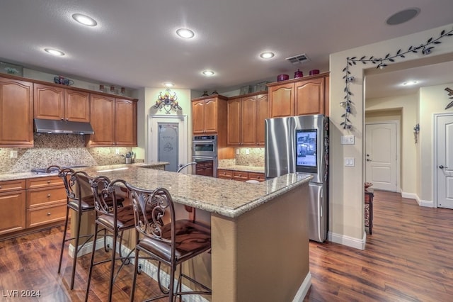 kitchen with appliances with stainless steel finishes, backsplash, a center island with sink, and a breakfast bar