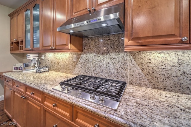 kitchen featuring under cabinet range hood, decorative backsplash, brown cabinets, and stainless steel gas cooktop