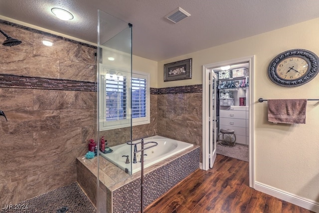 full bathroom featuring wood finished floors, visible vents, a tile shower, a textured ceiling, and a bath