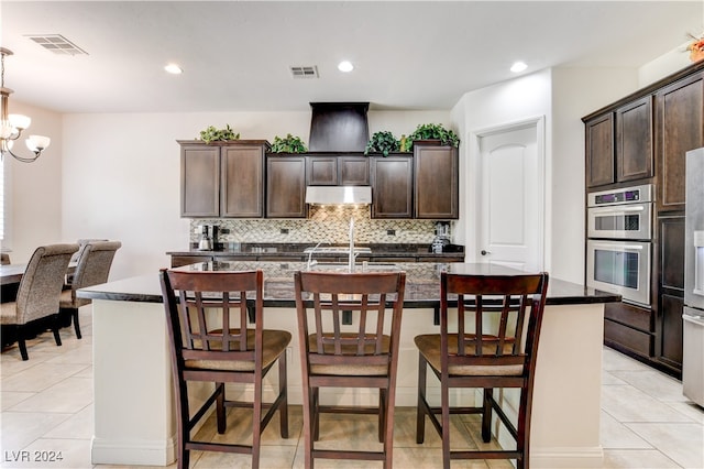 kitchen with a kitchen island with sink, dark stone countertops, a chandelier, decorative backsplash, and a breakfast bar