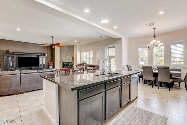 kitchen with a fireplace, ceiling fan with notable chandelier, sink, a center island with sink, and stainless steel dishwasher