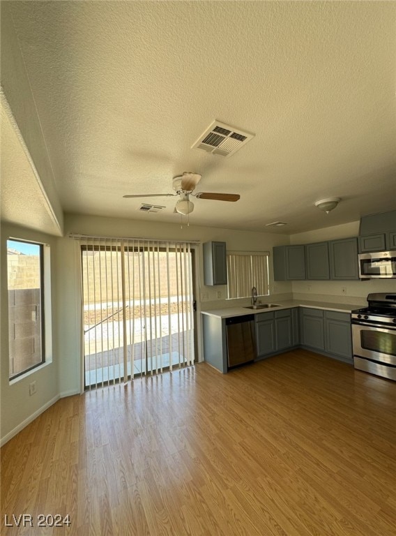 kitchen featuring appliances with stainless steel finishes, light hardwood / wood-style floors, sink, ceiling fan, and a textured ceiling