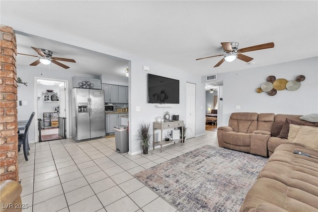 living area with ceiling fan, light tile patterned flooring, visible vents, and baseboards