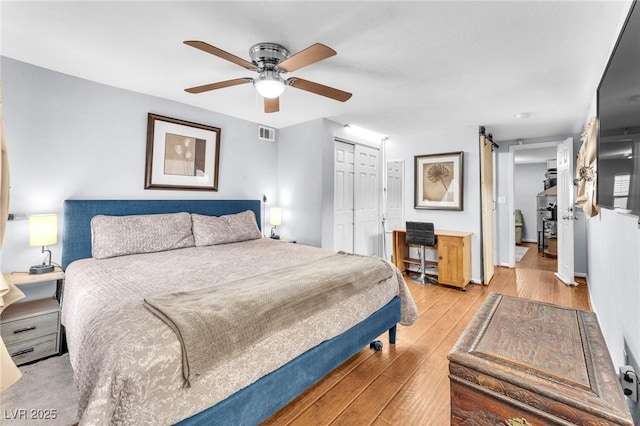 bedroom with a barn door, visible vents, light wood-style flooring, ceiling fan, and a closet