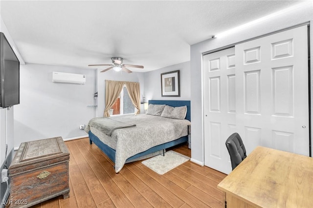 bedroom featuring a ceiling fan, baseboards, light wood-style floors, an AC wall unit, and a closet