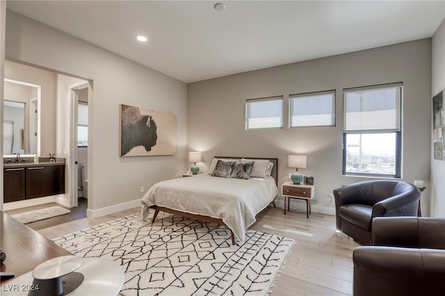 bedroom with light hardwood / wood-style flooring, connected bathroom, and sink