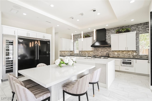 kitchen with hanging light fixtures, black refrigerator, wall chimney exhaust hood, a kitchen bar, and a center island with sink