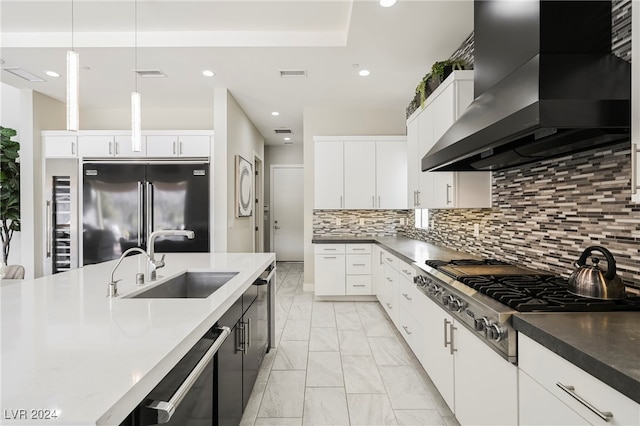 kitchen with pendant lighting, white cabinetry, stainless steel appliances, sink, and wall chimney exhaust hood