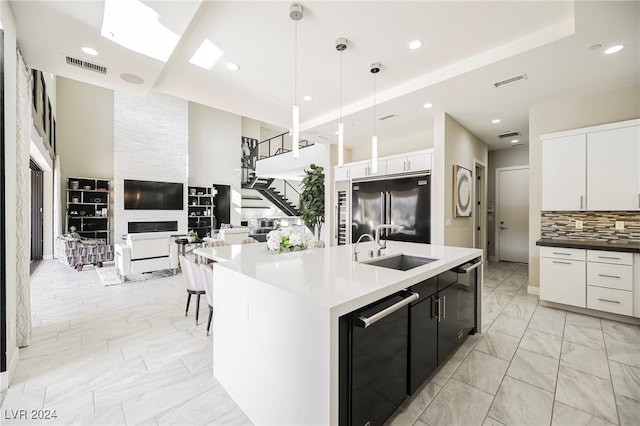 kitchen featuring built in refrigerator, decorative light fixtures, sink, a center island with sink, and white cabinets