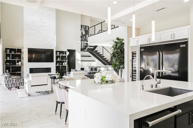 kitchen featuring a fireplace, sink, hanging light fixtures, stainless steel built in refrigerator, and white cabinets