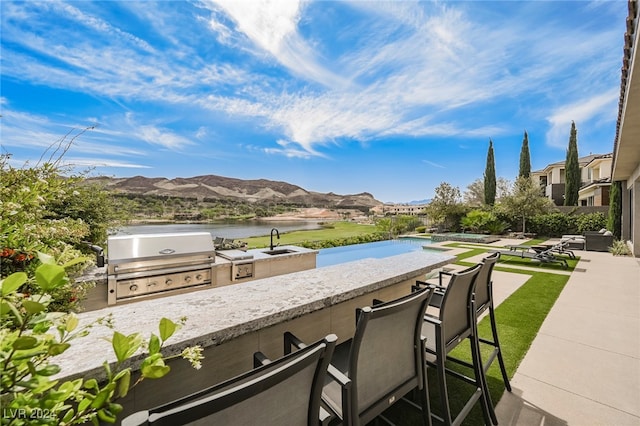 exterior space with exterior kitchen, grilling area, a water and mountain view, and sink