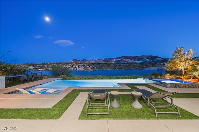 pool at twilight featuring a water and mountain view, a lawn, an in ground hot tub, and a patio area