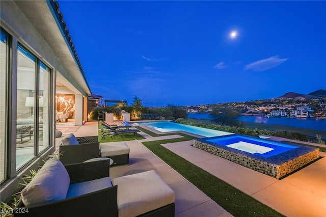 pool at night featuring a water view, a patio, outdoor lounge area, and an in ground hot tub