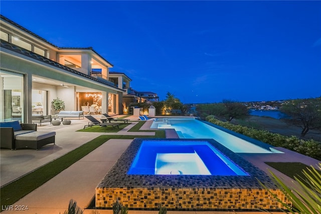 pool at night with outdoor lounge area, a patio area, and an in ground hot tub