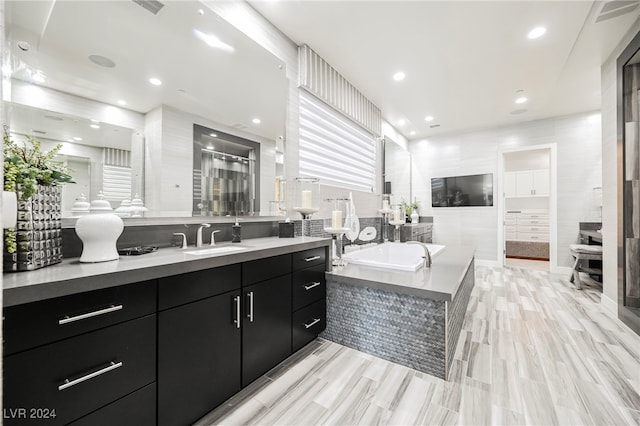 bathroom with tiled tub, vanity, and tile walls