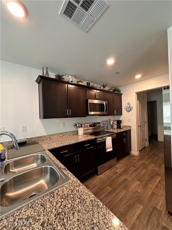 kitchen featuring appliances with stainless steel finishes, light stone countertops, dark hardwood / wood-style floors, dark brown cabinetry, and sink