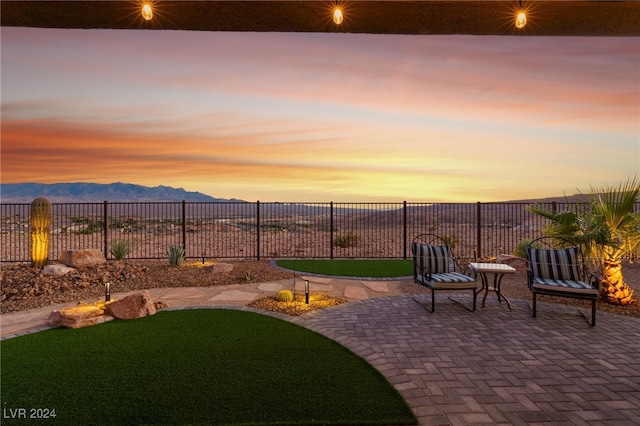 patio terrace at dusk featuring a mountain view and a lawn