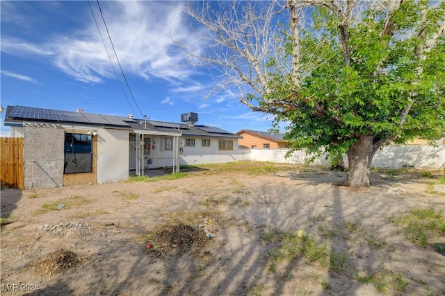 back of house featuring solar panels, fence, and stucco siding