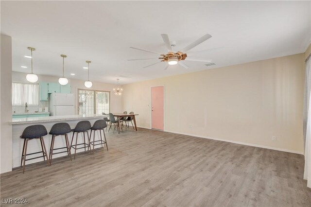 kitchen featuring kitchen peninsula, ceiling fan with notable chandelier, white refrigerator, decorative light fixtures, and light hardwood / wood-style floors