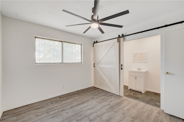 unfurnished bedroom featuring ensuite bathroom, ceiling fan, sink, wood-type flooring, and a barn door