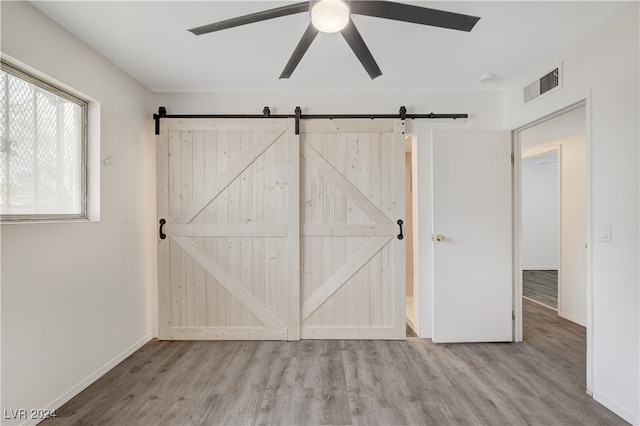 unfurnished bedroom featuring ceiling fan, a barn door, and light hardwood / wood-style floors