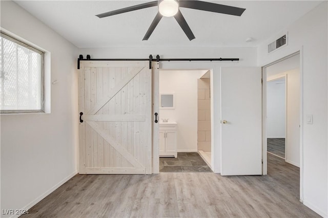 unfurnished bedroom with a barn door, wood finished floors, visible vents, and ensuite bathroom