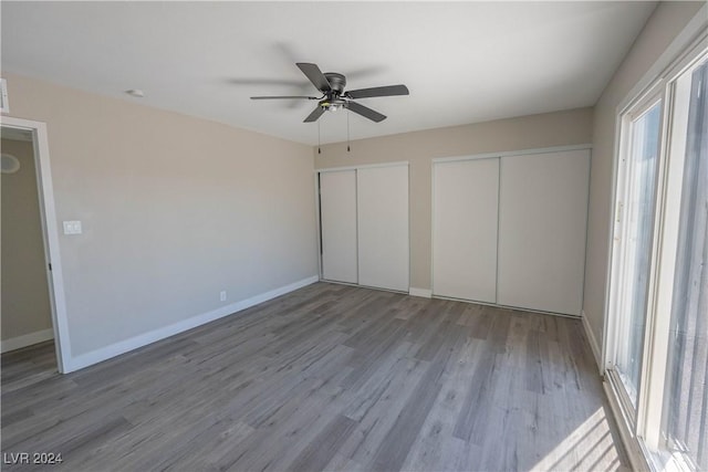 unfurnished bedroom featuring baseboards, wood finished floors, and multiple closets