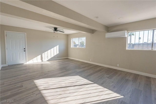 unfurnished room featuring an AC wall unit, beamed ceiling, baseboards, and wood finished floors