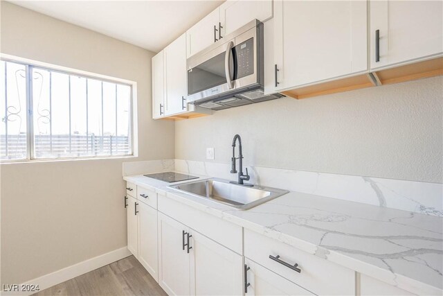 kitchen with white cabinetry, light hardwood / wood-style flooring, sink, and light stone countertops