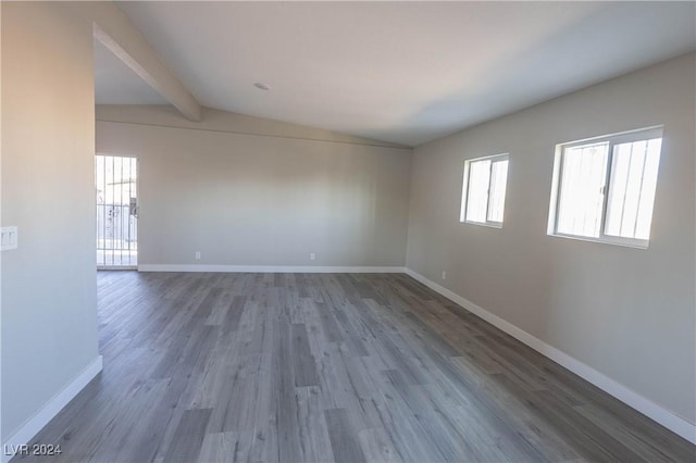 unfurnished room featuring lofted ceiling with beams, baseboards, and wood finished floors