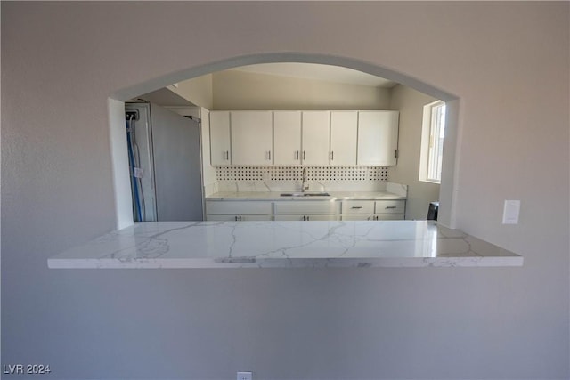 kitchen with arched walkways, light stone counters, a sink, white cabinetry, and tasteful backsplash