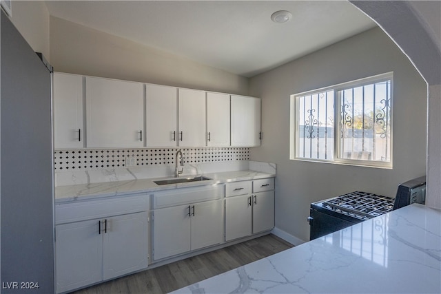 kitchen with gas stove, light wood-type flooring, light stone countertops, white cabinetry, and sink