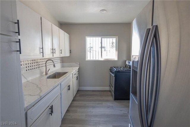 kitchen featuring light wood-type flooring, light stone counters, stainless steel appliances, white cabinetry, and sink