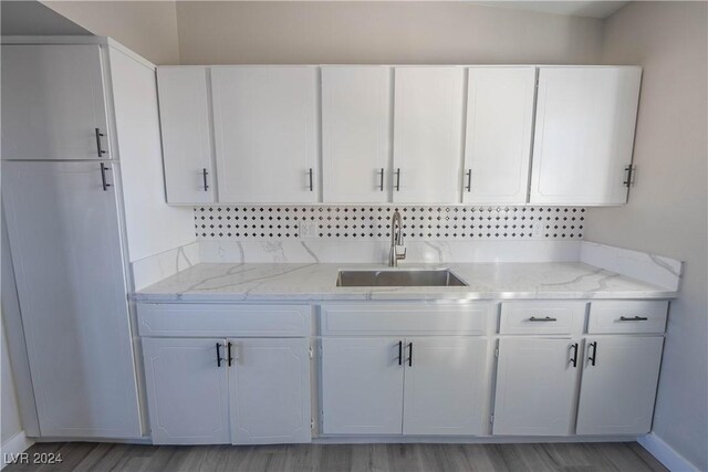 kitchen with light stone counters, sink, white cabinetry, and light hardwood / wood-style floors