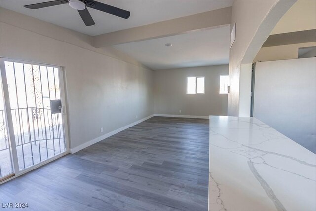 spare room featuring a healthy amount of sunlight, ceiling fan, hardwood / wood-style flooring, and lofted ceiling with beams