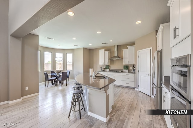 kitchen with a breakfast bar area, sink, wall chimney range hood, light wood-type flooring, and white cabinets