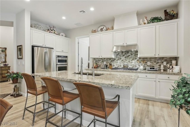 kitchen featuring tasteful backsplash, an island with sink, light hardwood / wood-style flooring, and white cabinets