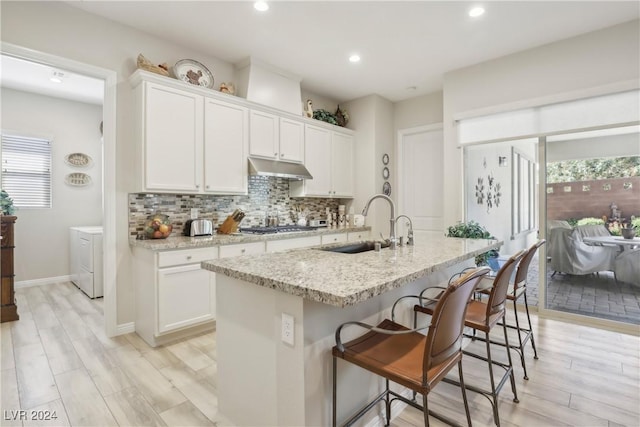 kitchen featuring sink, tasteful backsplash, light stone counters, a center island with sink, and white cabinets